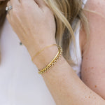 Close-up of a person's arm wearing two gold bracelets on a blurred background