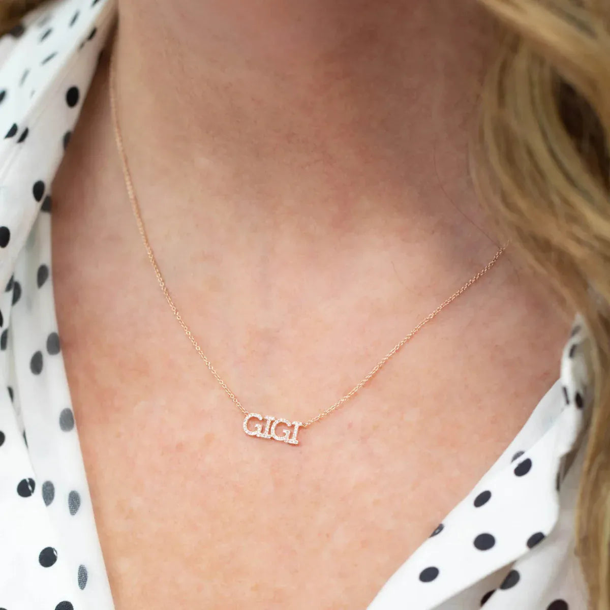 Close-up of a blonde woman's décolletage wearing a rose gold Pavé GIGI Necklace with cable chain, wearing a white and black polka dot blouse. 