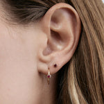 Close-up of a Birthstone Stud and Birthstone Hoop - Ruby (July) in a woman's ear,  with her brown hair visible. 