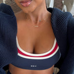 Person wearing a navy sports bra with red and white stripes and a navy cardigan and wearing a zodiac gold neclace and 4 charm gold necklace