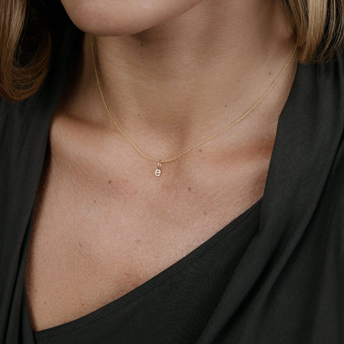Close-up of a woman's neck wearing a Signature Cable Chain with a Petite Letter Charm in e, styled in a black top. 