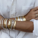 Close-up of arms wearing silver and god Rendezvous Cuffs, Plus One Cuffs and All In Cuffs, a C'est Moi Link Ring and an Open Diamond Ring,  styled with a white shirt. 