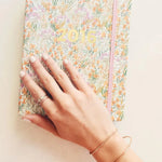 A hand wearing a Simple Bangle and a Diamond Cut Bracelet in rose gold and two rings, placed on top of a floral 2016 notebook.