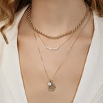Close-up of a woman's décolletage wearing a Rolo Necklace, a Diamond Arc Layering Necklace and The Slide Chain with a Spark Sign Jumble, all in yellow gold, with a white top. 