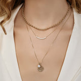 Close-up of a woman's décolletage wearing a Rolo Necklace, a Diamond Arc Layering Necklace and The Slide Chain with a Spark Sign Jumble, all in yellow gold, with a white top. 