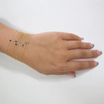 A hand wearing multiple Birthstone Bracelets stacked with different stones on a white background. 