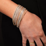 A hand wearing several white gold and yellow gold Love Set Match Bracelets and Down the Line Bracelets, and several yellow gold rings against black background. 