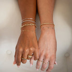 Two hands wearing several bracelets and rings in yellow and white gold: a Bold Link Bracelet, an Element Long Link Bracelet, two BFF Bracelets, a Down the Line Bracelet, a Love Set Match Bracelet, a Geo Stacking Ring, an Etched Paris Ring, a Link Ring and an Open Diamond Ring, against a neutral background.