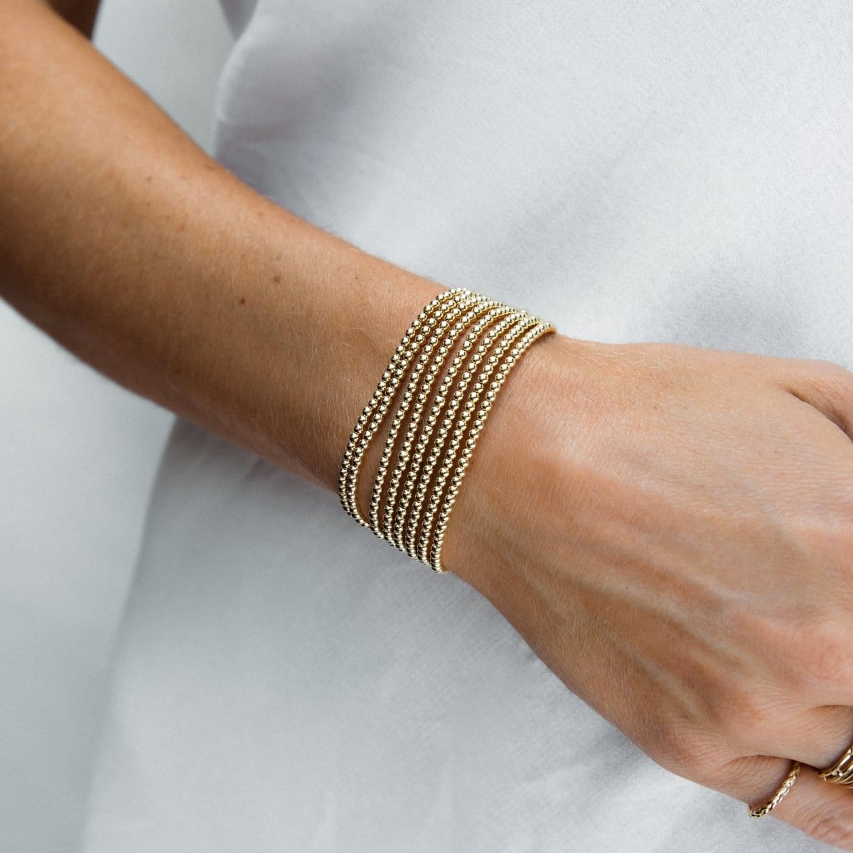 A close-up of a woman's wearing multiple Classic Beaded Bracelets stacked, with a white top. 