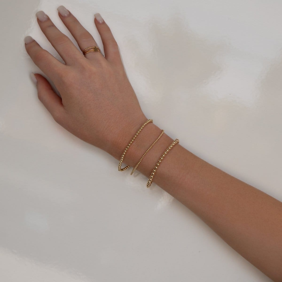 A hand wearing a Classic Bubble Bracelet Set, two Delicate Beaded Bands and a Twinkle Twinkle ring against a neutral background.