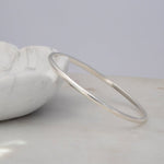 A sterling silver Flirt Bangle against a light marble bowl and a light grey surface. 