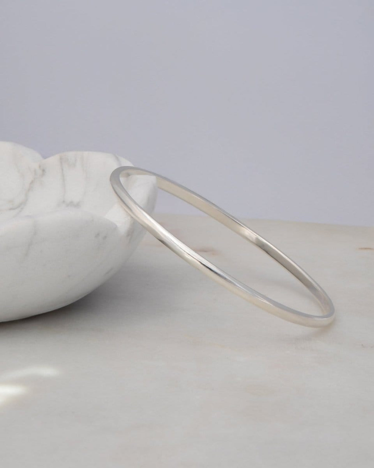 A sterling silver Flirt Bangle against a light marble bowl and a light grey surface. 