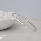 A sterling silver Flirt Bangle against a light marble bowl and a light grey surface. 