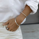 An arm wearing a silver Flirt Bangle and For Keeps Bangle and a white gold Etched Paris Ring, styled in a white shirt and off-white pants. 