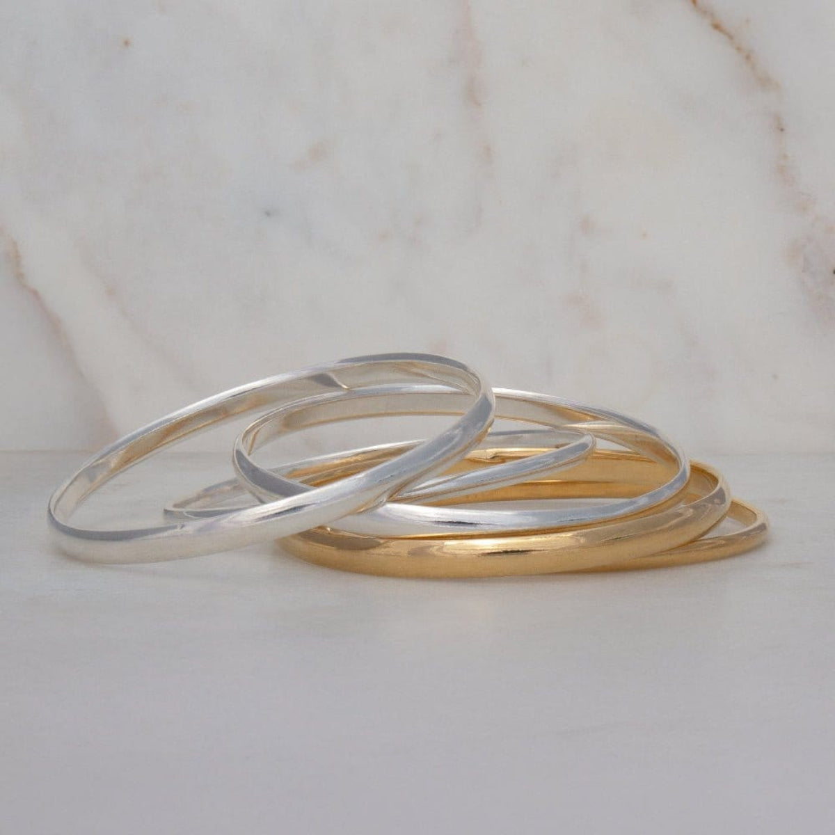 Several silver and gold For Keeps Bangles on a light marble surface. 