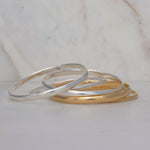 Several silver and gold For Keeps Bangles on a light marble surface. 