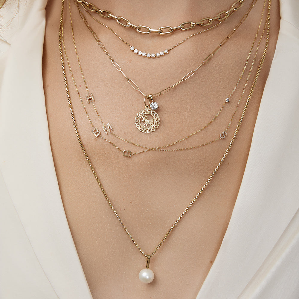 Multiple gold necklaces with various pendants on a person wearing a white outfit.