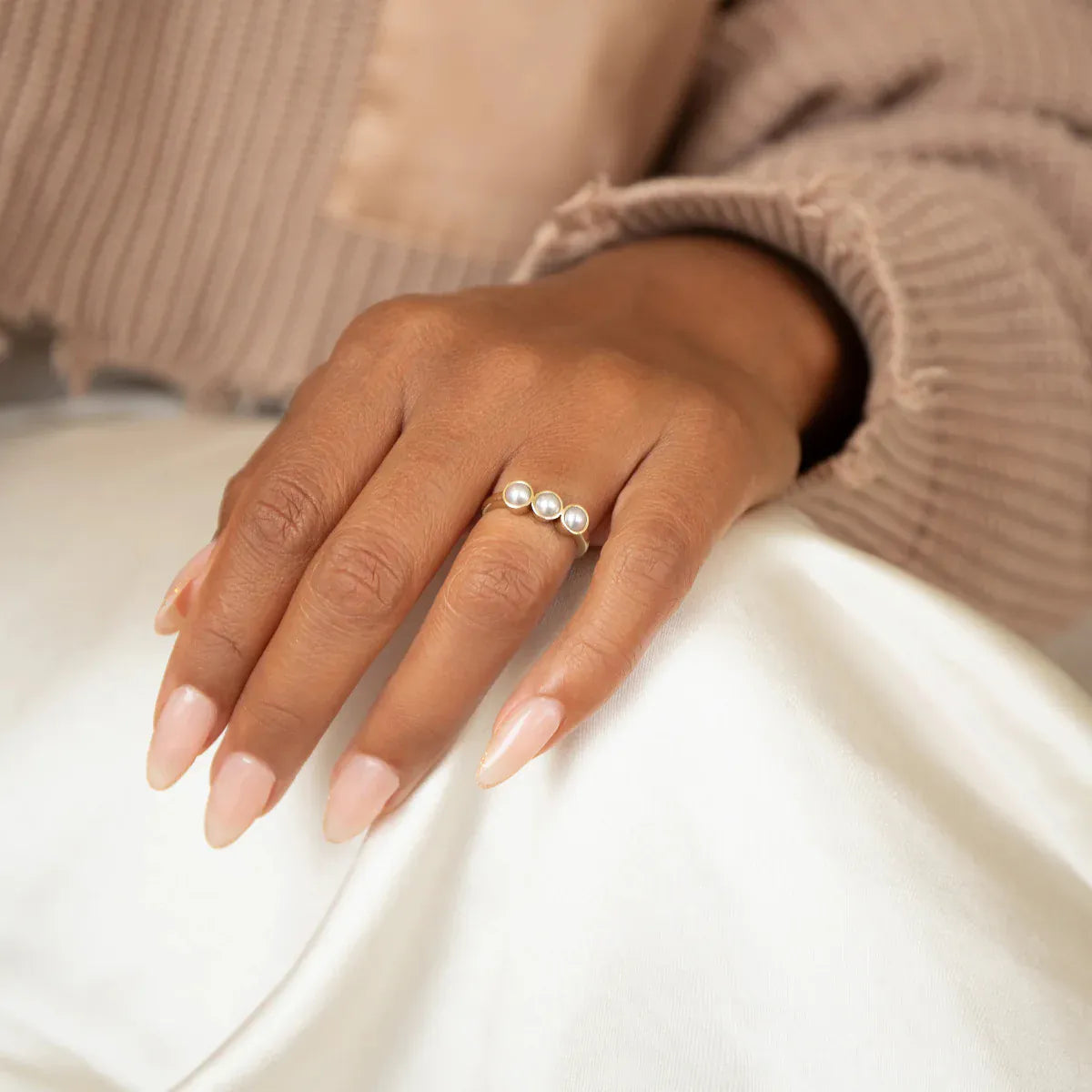 A woman's hand wearing a Tres Pearl Ring resting on her white pants in a neutral top. 