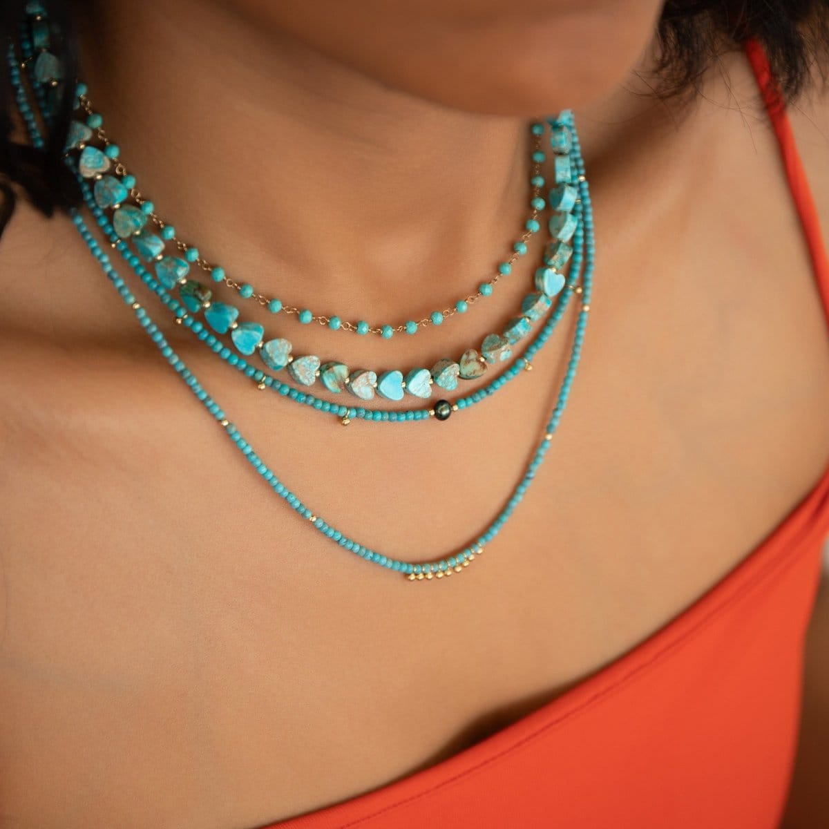 Close-up of a neck wearing The Bluebell Bouquet Necklace and Endless Summer Necklaces in Santorini, Turqs + Caicos, and Sea + Sky, styled with a red top.
