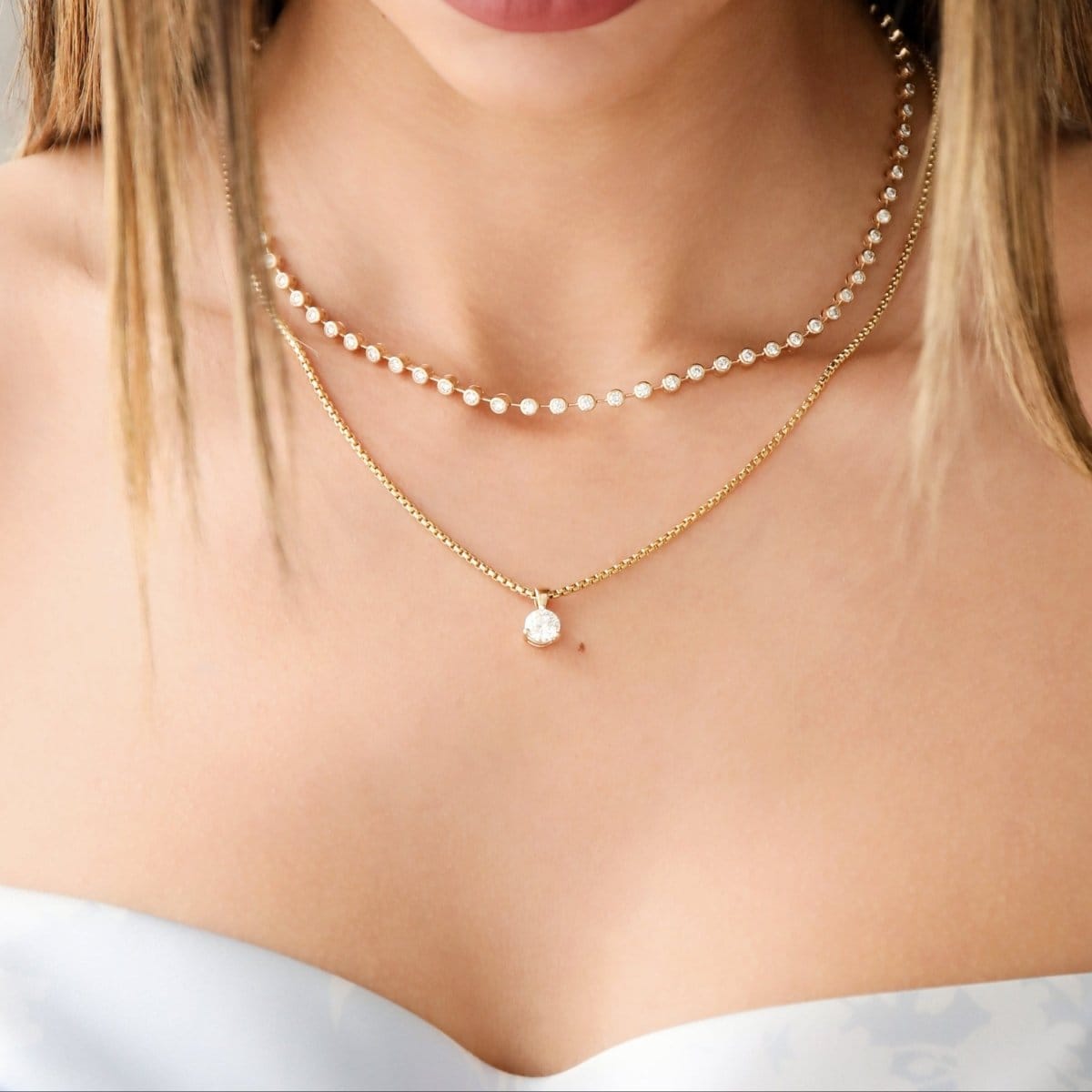 Close-up of a decolletage wearing The Ultimate Diamond Necklace and a Box Chain with a Queen Diamond Pendant, with a light blue strapless top. 
