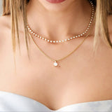 Close-up of a decolletage wearing The Ultimate Diamond Necklace and a Box Chain with a Queen Diamond Pendant, with a light blue strapless top. 