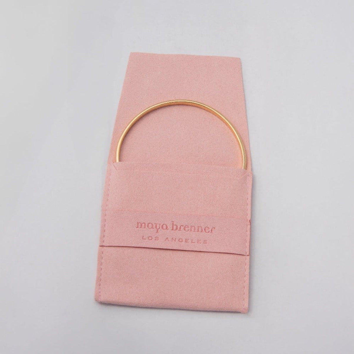 A gold vermeil Flirt Bangle inside a pink Maya Brenner jewellery pouch. 