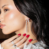 A woman wearing a Love on the Rocks Ring, a Make It a Double Ring, a Triple Sec Diamond Earring and a Diamond Cascade Earring, all in white gold, with red nails and black hair.