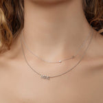 A close-up of a woman's neck wearing a Monogram Necklace with Diamond White Gold with the letter S and a white gold MIMI Necklace. 