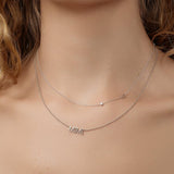 A close-up of a woman's neck wearing a Monogram Necklace with Diamond White Gold with the letter S and a white gold MIMI Necklace. 