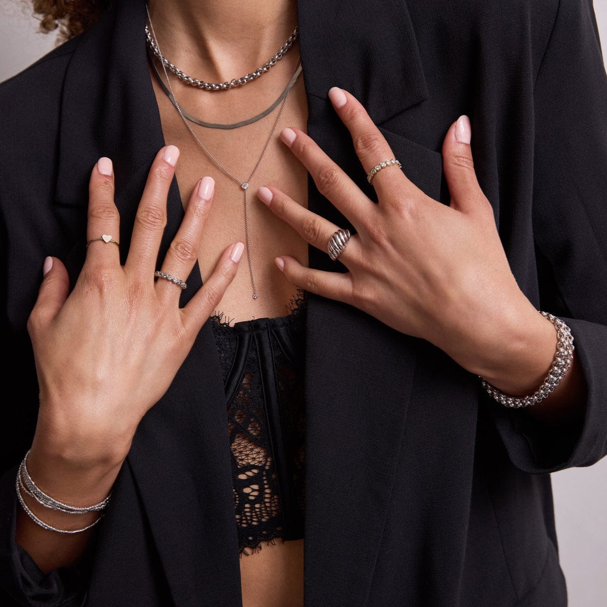A woman wearing a Rolo Necklace, Sequence Chain, Diamond Drip Necklace, several Rolo Bracelets and Diamond Cut Bracelets, two The Evermore Rings, an Etched Paris Ring and a Heartfelt Ring, styled in a black lace top and blazer.