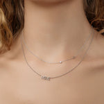 Close-up of a woman's décolletage wearing a Custom Gold Necklace - 2 Letters (an S and a diamond) and a MIMI Necklace with a bead chain, both in white gold, with blonde curly hair visible. 