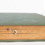 A white gold Pavé Charm Stud - Moon and Birthstone Stud - Amethyst  in a book against a white background. 