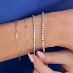 A close-up of a wrist wearing an Element Short Link Bracelet, an Element Long Link Bracelet, a Down the Line Bracelet and a Love Set Match Bracelet, against a blue background.