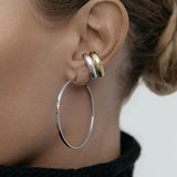 Close-up of an ear wearing two Ready to Mingle Ear Cuffs, one in yellow gold and the other in white gold, and a Sleek & Chic Hoop - Medium in white gold, against a white blurred background. 