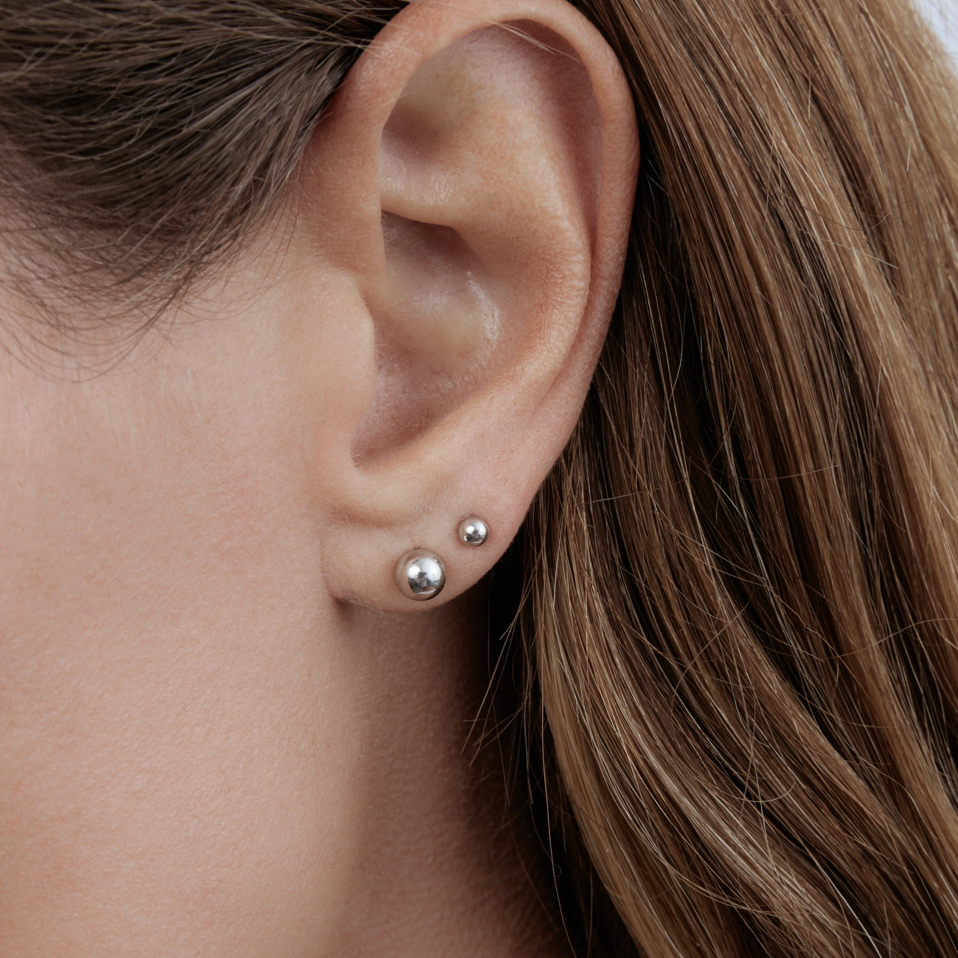 Close-up of an ear with white gold post earrings against a neutral background