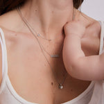 Woman wearing a 'MAMA' necklace with a baby's hand on her chest.