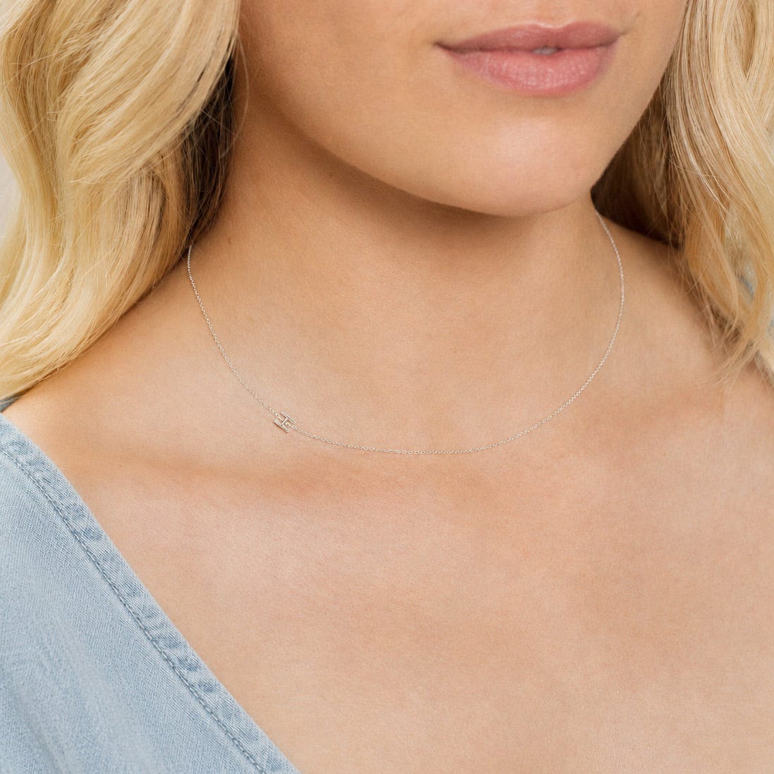 Close-up of a woman's neck wearing a white gold necklace with a letter H charm.
