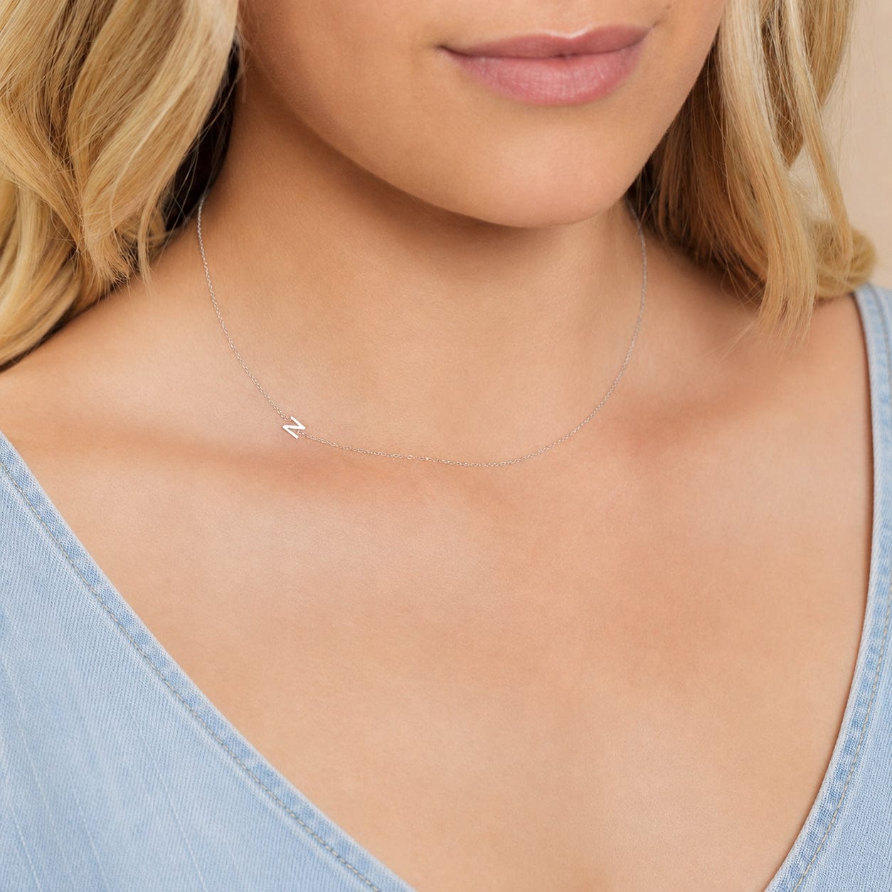 Close-up of a woman's neck wearing a white gold necklace with a letter N charm.