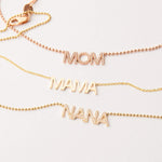 A Pavé MOM Necklace in rose gold, a MAMA Necklace in yellow gold and a  Pavé MOM Necklace in yellow gold, on an off-white background. 