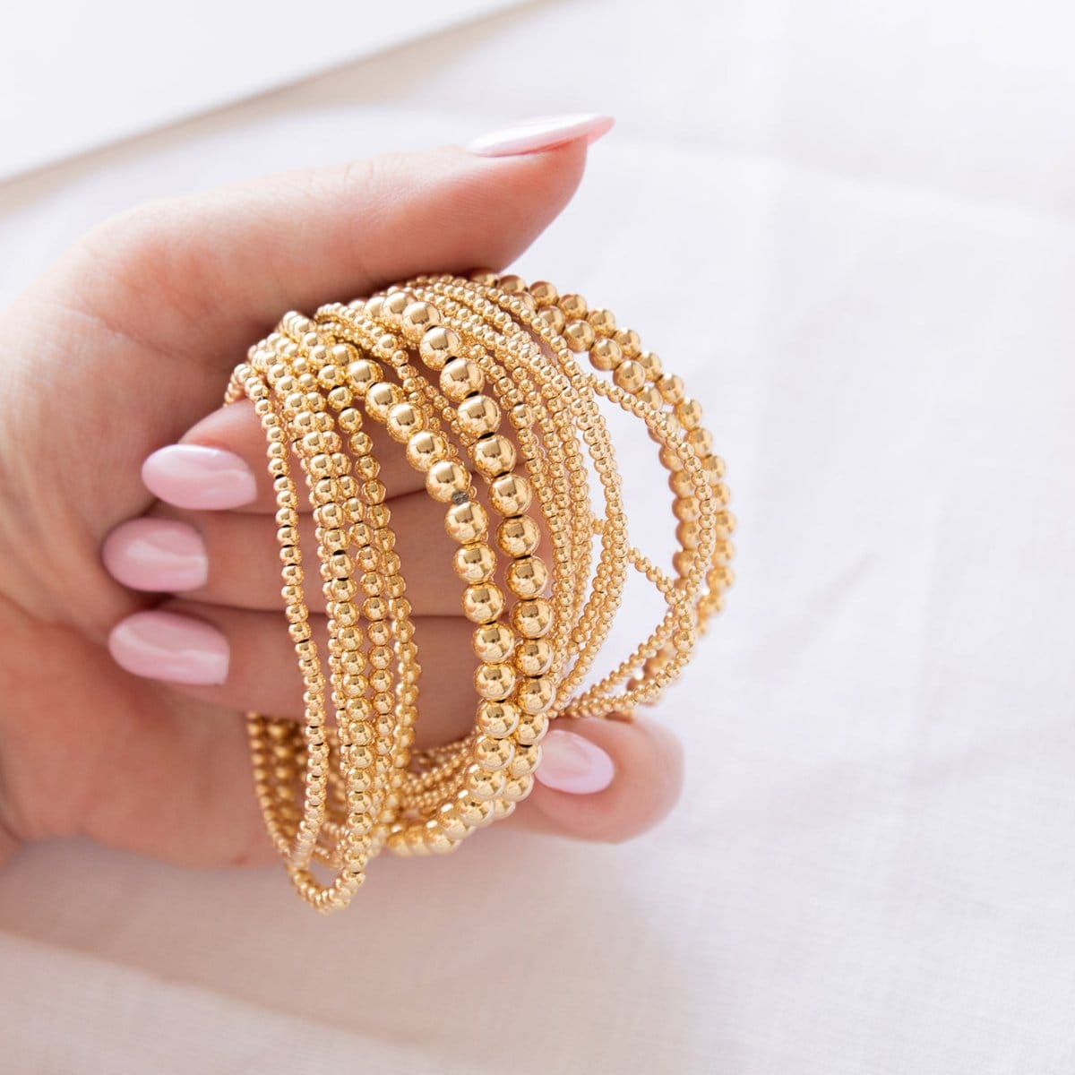 A hand holding multiple yellow gold Bubble Bracelets in various sizes against a white background. 