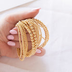 A hand holding multiple yellow gold Bubble Bracelets in various sizes against a white background. 