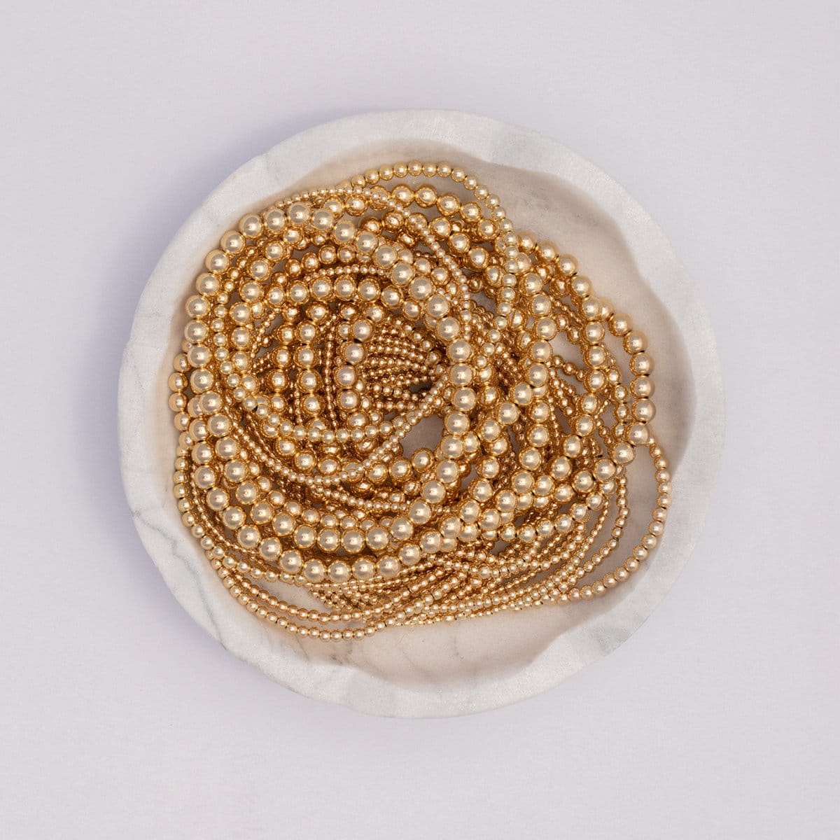 Yellow gold Bubble Bracelets in various sizes coiled in a white marble bowl, against a white background.