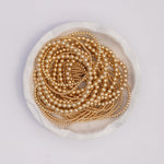 Yellow gold Bubble Bracelets in various sizes coiled in a white marble bowl, against a white background.