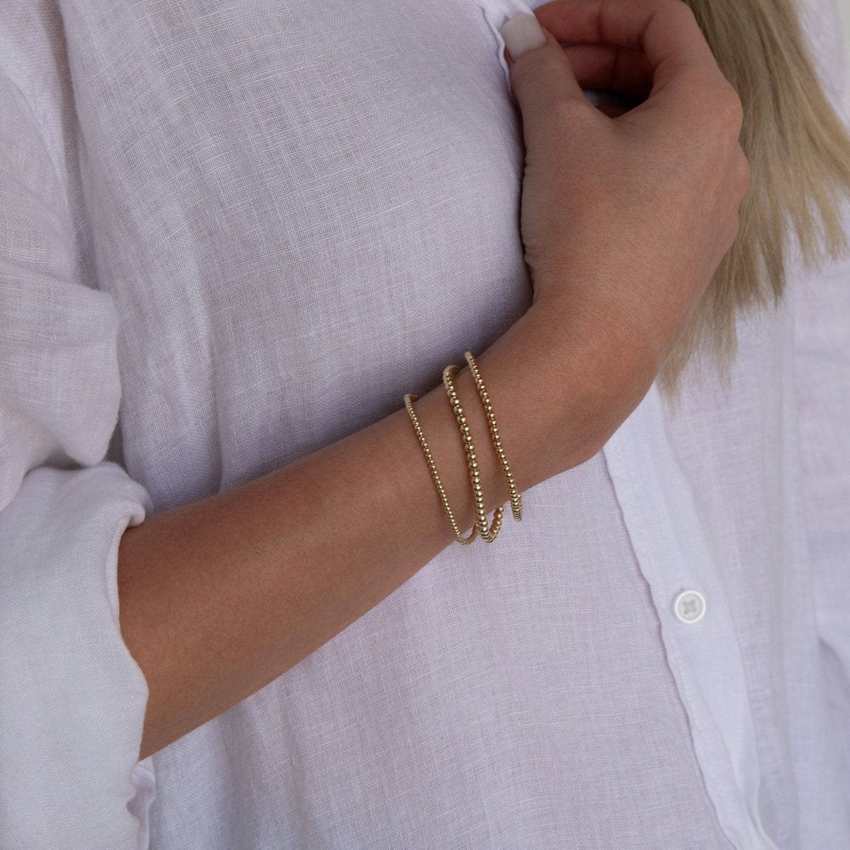 A woman’s arm wearing the Dainty Bubble Bracelet Set in yellow gold, with a white shirt.