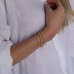 A woman’s arm wearing the Dainty Bubble Bracelet Set in yellow gold, with a white shirt.