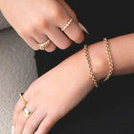 A close-up of a woman’s hands wearing two Rolo Bracelets, an Evermore Ring, an Etched Paris Ring, a Geo Stacking Ring and a Thick Band, against a black knit dress.