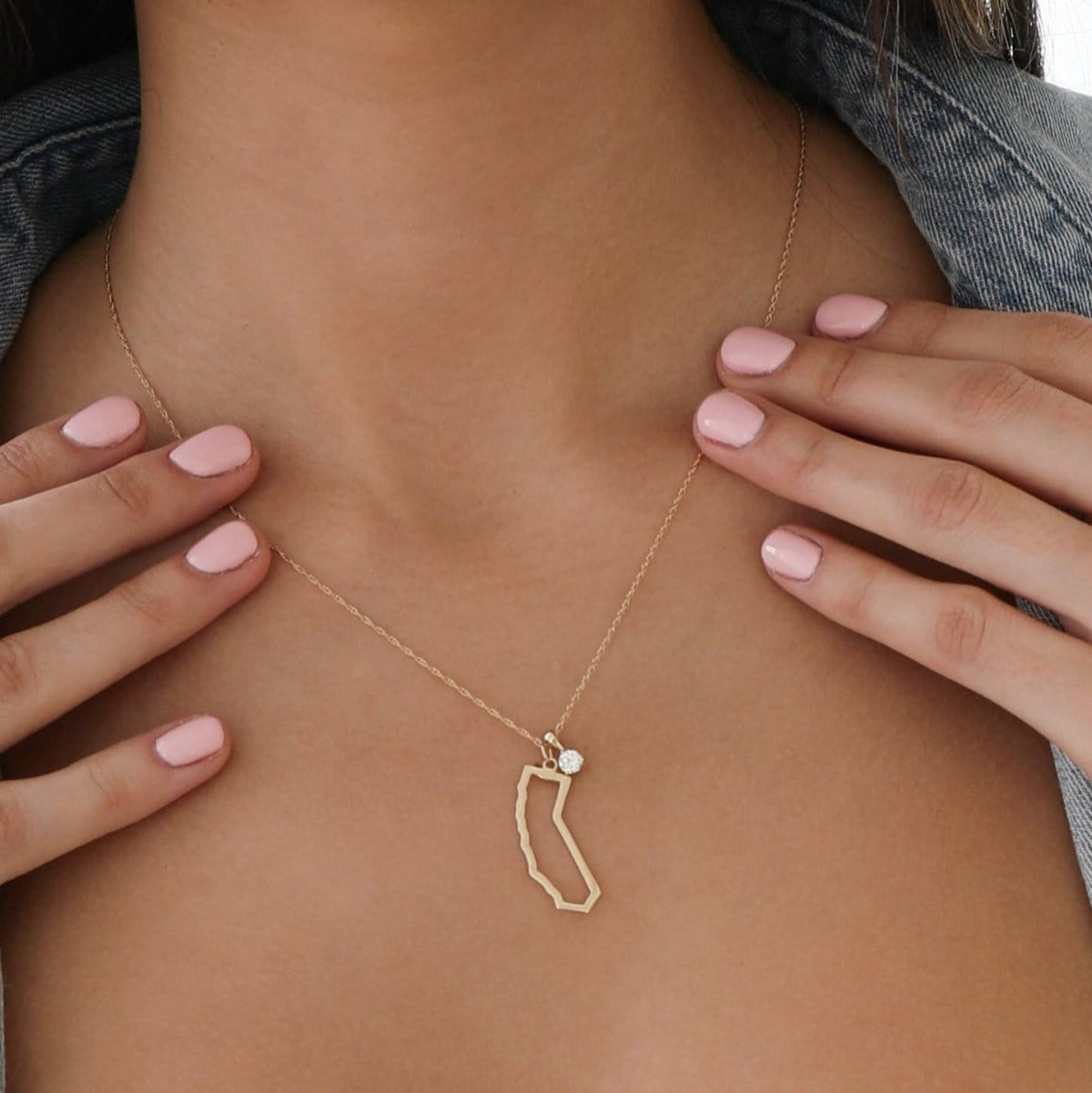 Close-up of a woman's decellotage wearing a California Necklace with a Duchess Diamond Pendant, held by her hands with light pink nails. 