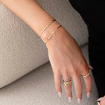 A hand wearing two Off the Cuff Bracelets, an Etched Paris Ring and The Evermore Ring, all in yellow gold, against a neutral background. 