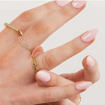 Hand wearing Delicate Trio Stacking Rings, a Birthstone Ring, two Pavé Diamond Rings,  Geo Stacking Ring Square, with pink nail polish on a light grey background.