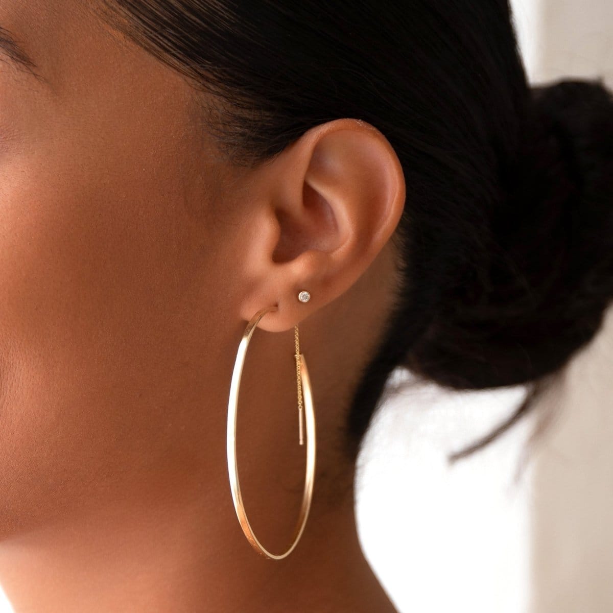 Close-up of an ear wearing a Sleek & Chic Hoop - Large and a Birthstone Stud - Diamond against a light blurred background. 